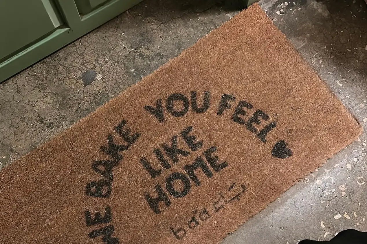 سجادة عند باب باء مكتوب عليها WE BAKE YOU FEEL LIKE HOME